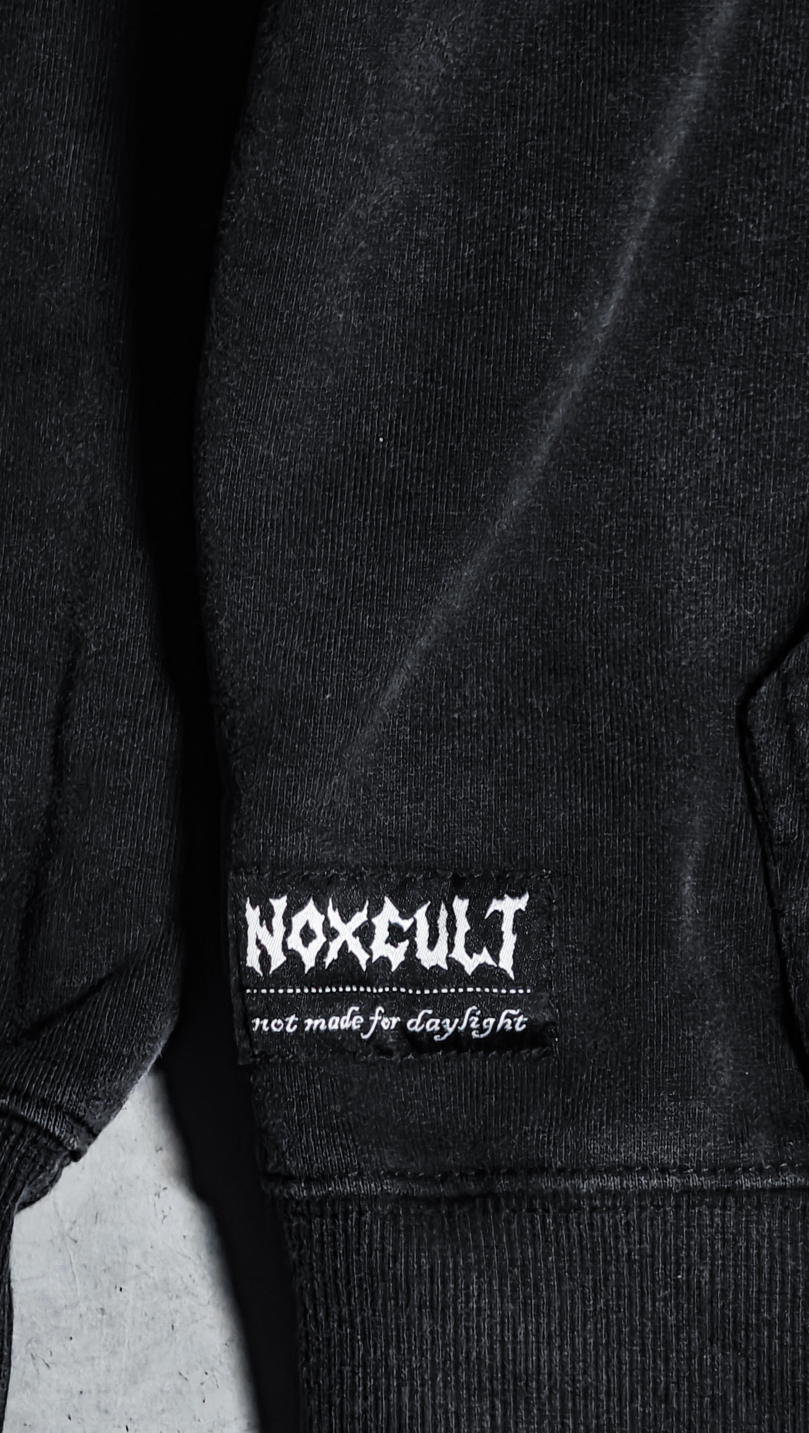 Détail étiquette tissée NOXCULT sur hoodie MONARCH — charm zinc forgé et zip laiton gun metal

